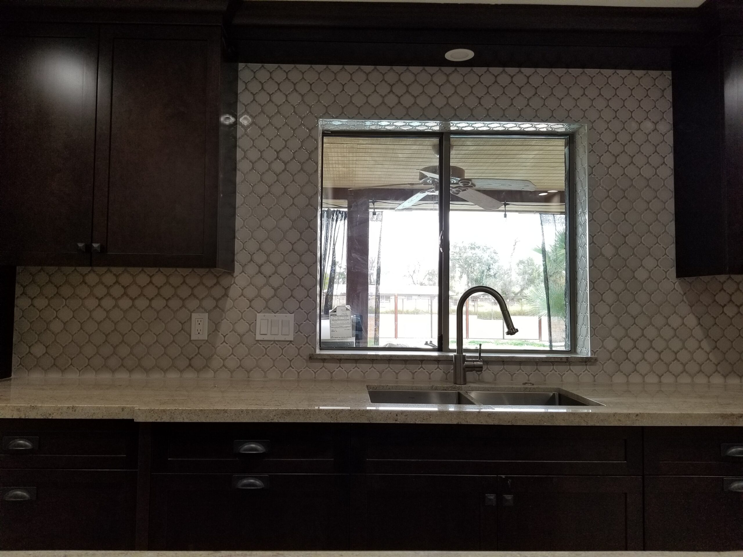 Contemporary Mesa kitchen detail featuring dark brown cabinetry, a stainless steel sink, a chrome faucet, a light countertop, and a decorative mosaic backsplash with a view outside.