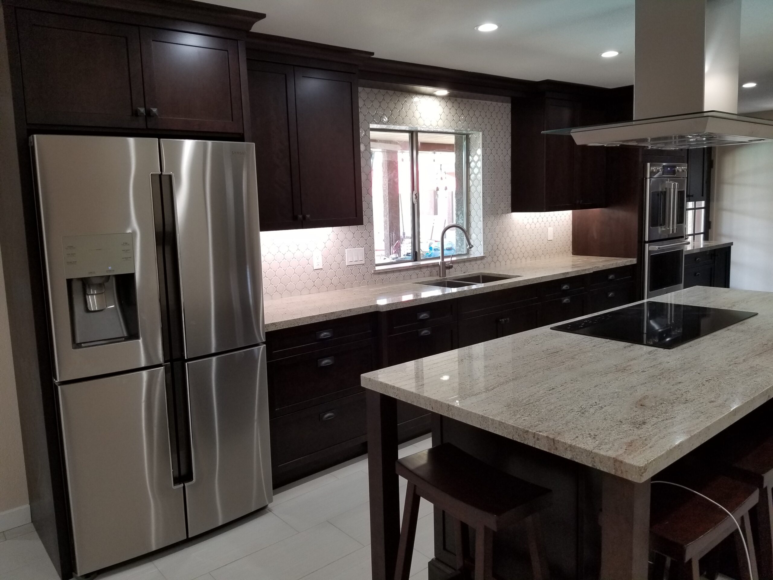 Modern kitchen in a Mesa, Arizona home with dark espresso cabinets, a light granite countertop island, stainless steel Samsung refrigerator, and a mosaic tile backsplash.