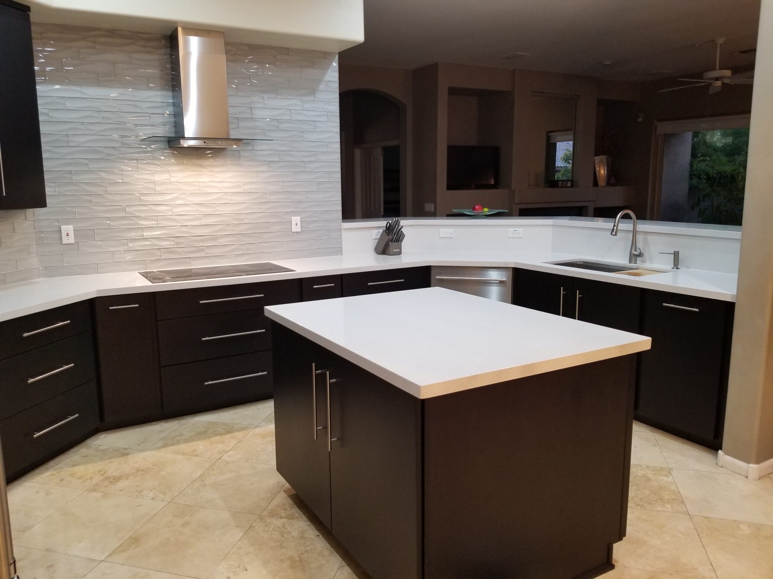 Modern kitchen in a Tempe home with dark espresso cabinets, a white countertop island, stainless steel appliances, and a textured backsplash.