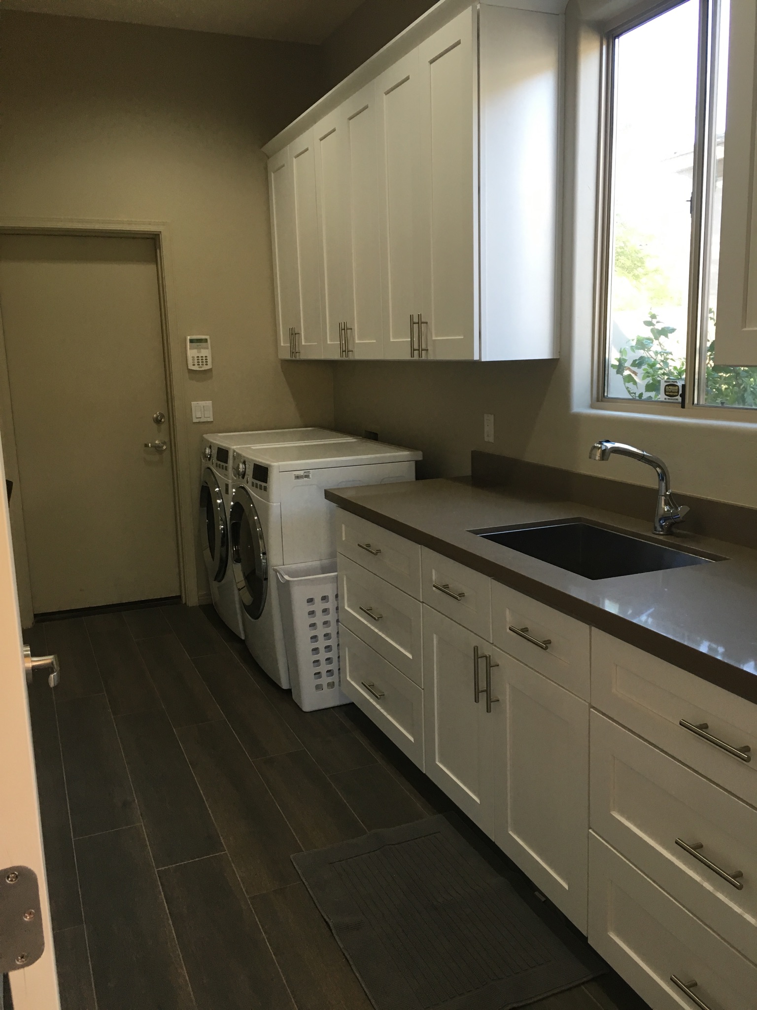 Modern laundry room in a Tempe home with white cabinets, a dark countertop, stainless steel sink, and white washing machine and dryer.