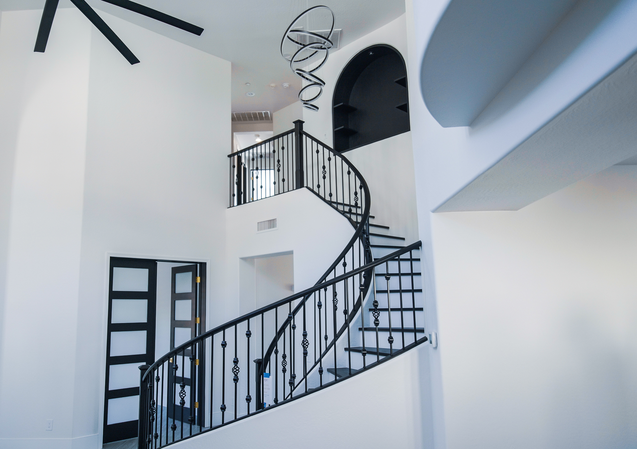 Elegant wrought iron spiral staircase in a bright, two-story entryway of a Tempe home, illuminated by an Artemide Alphabet of Light chandelier.