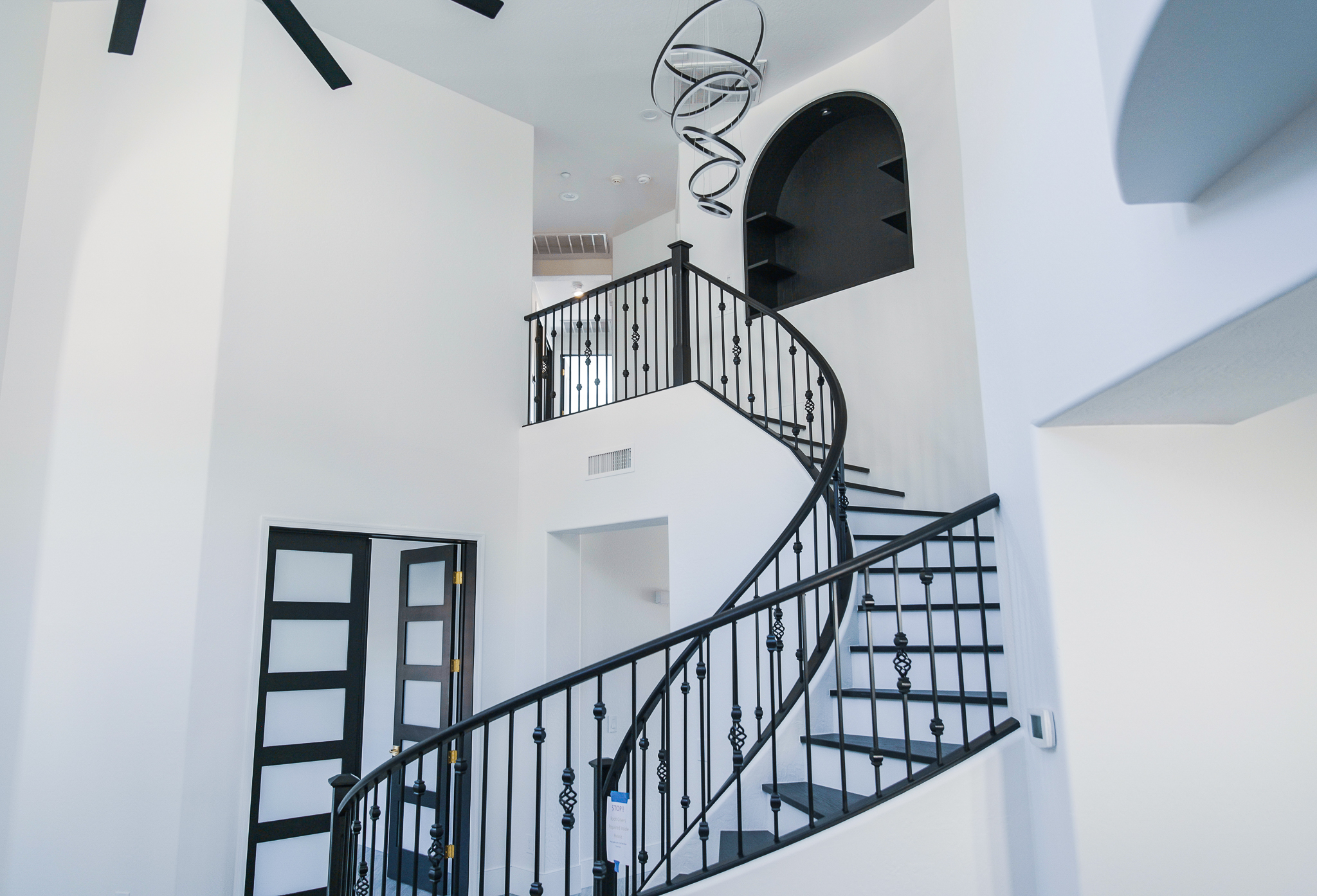 Wide view of a modern Tempe entryway featuring a wrought iron spiral staircase, a black Minka-Aire ceiling fan, and an Artemide Alphabet of Light chandelier.