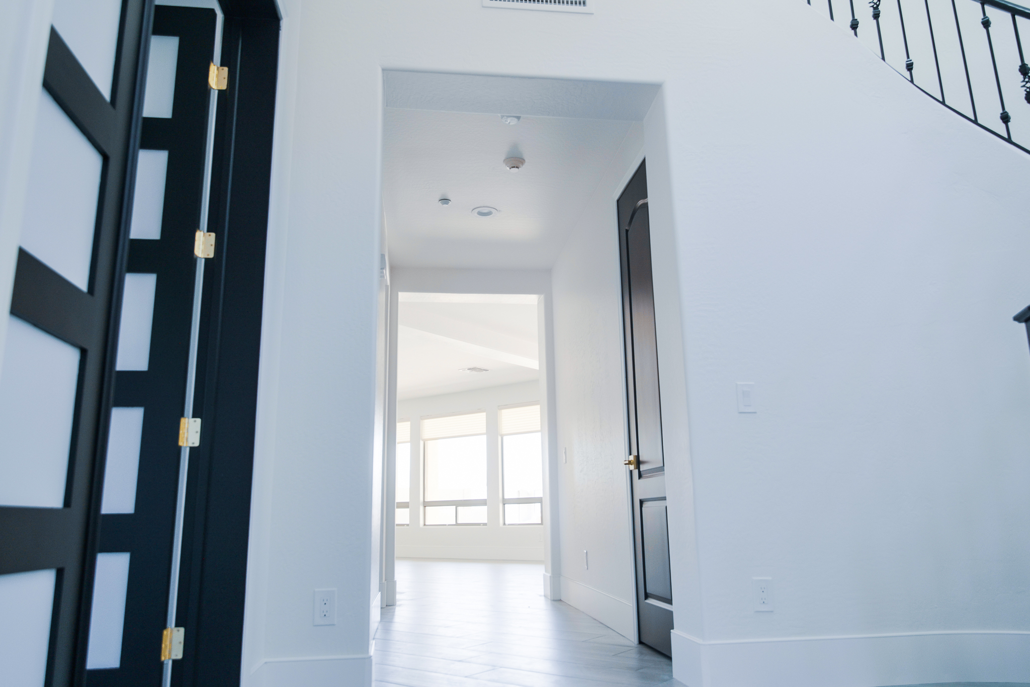 Modern interior hallway with white walls, light flooring, and a partially visible black patterned door.