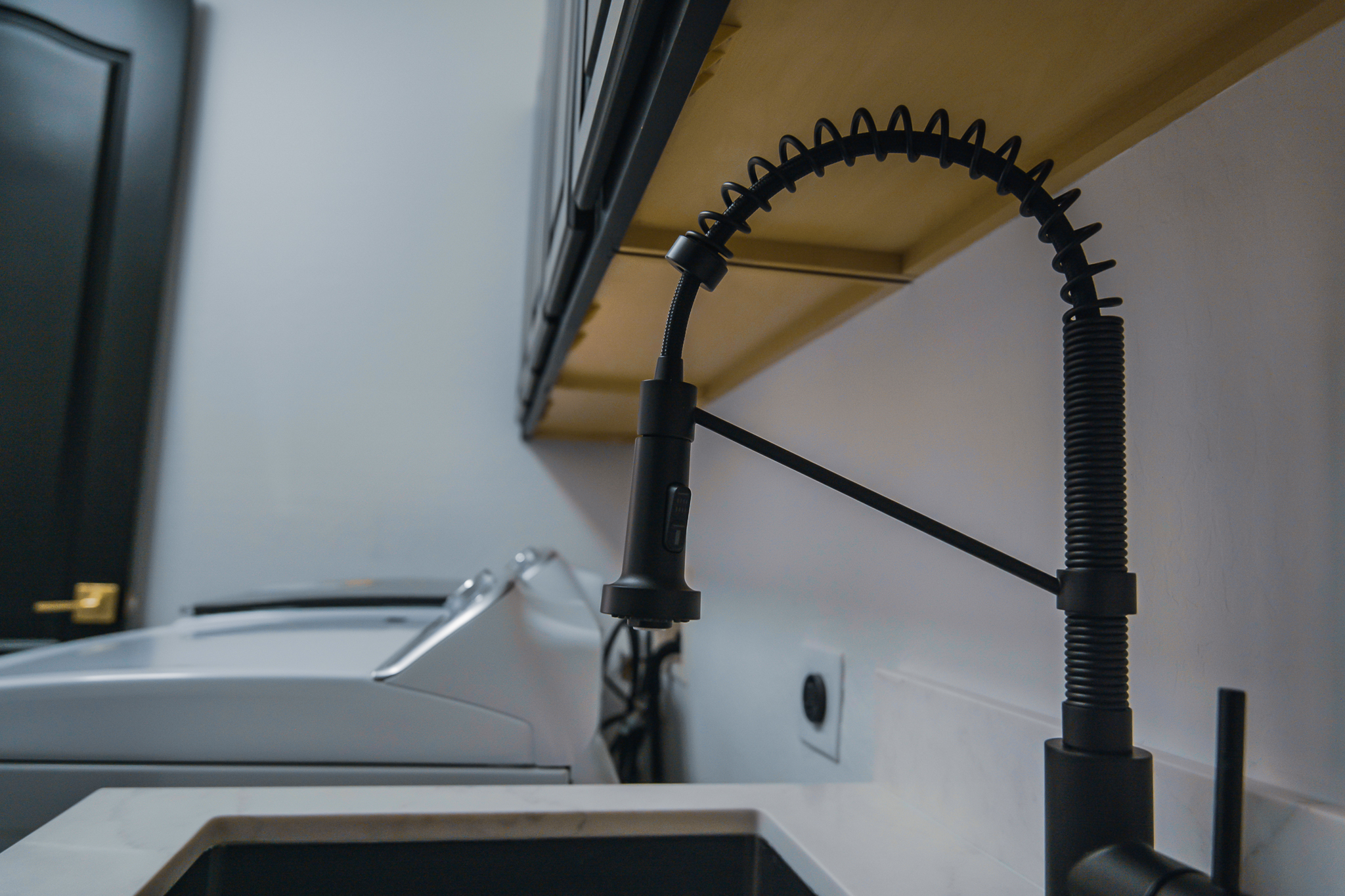 Modern black pull-down kitchen faucet over a dark sink, with a washing machine in the background.