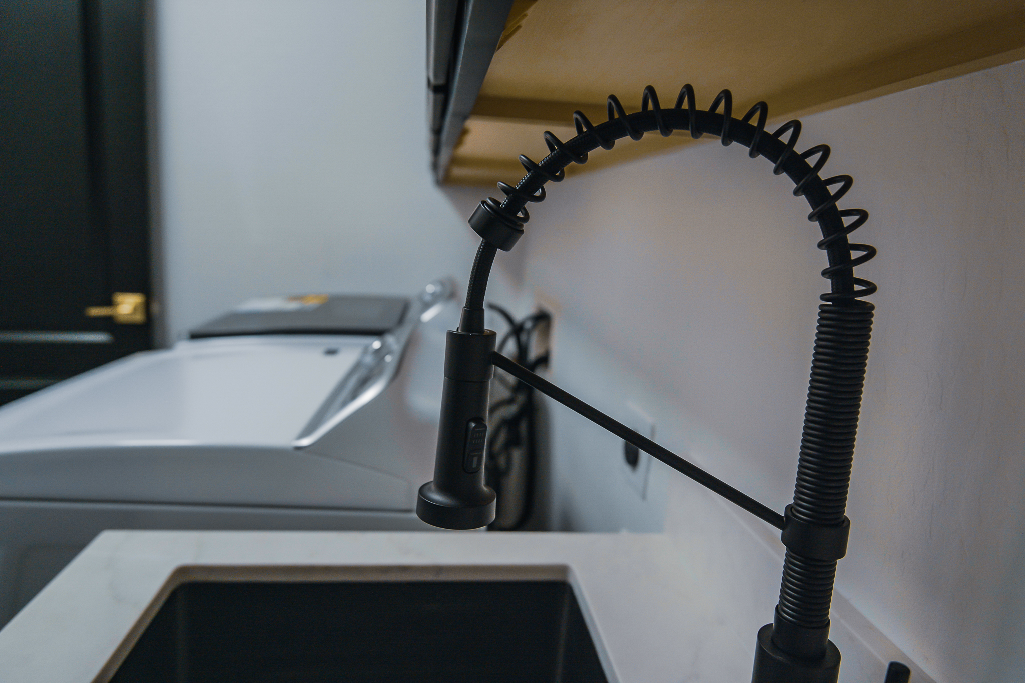 Modern black pull-down kitchen faucet over a dark sink, with a washing machine in the background.