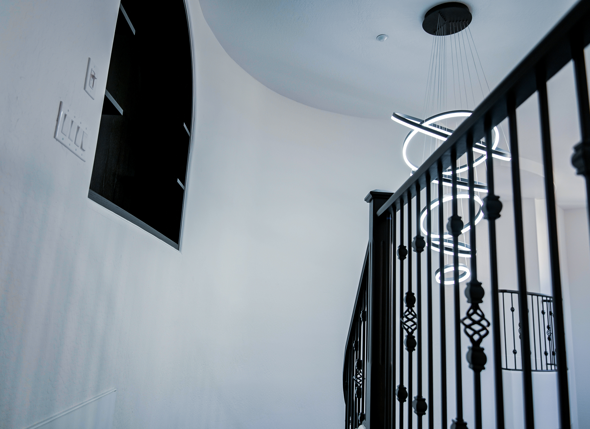 Unique, spiraling LED pendant light with eight interconnected, glowing rings creates a contemporary focal point in a sunlit stairwell.