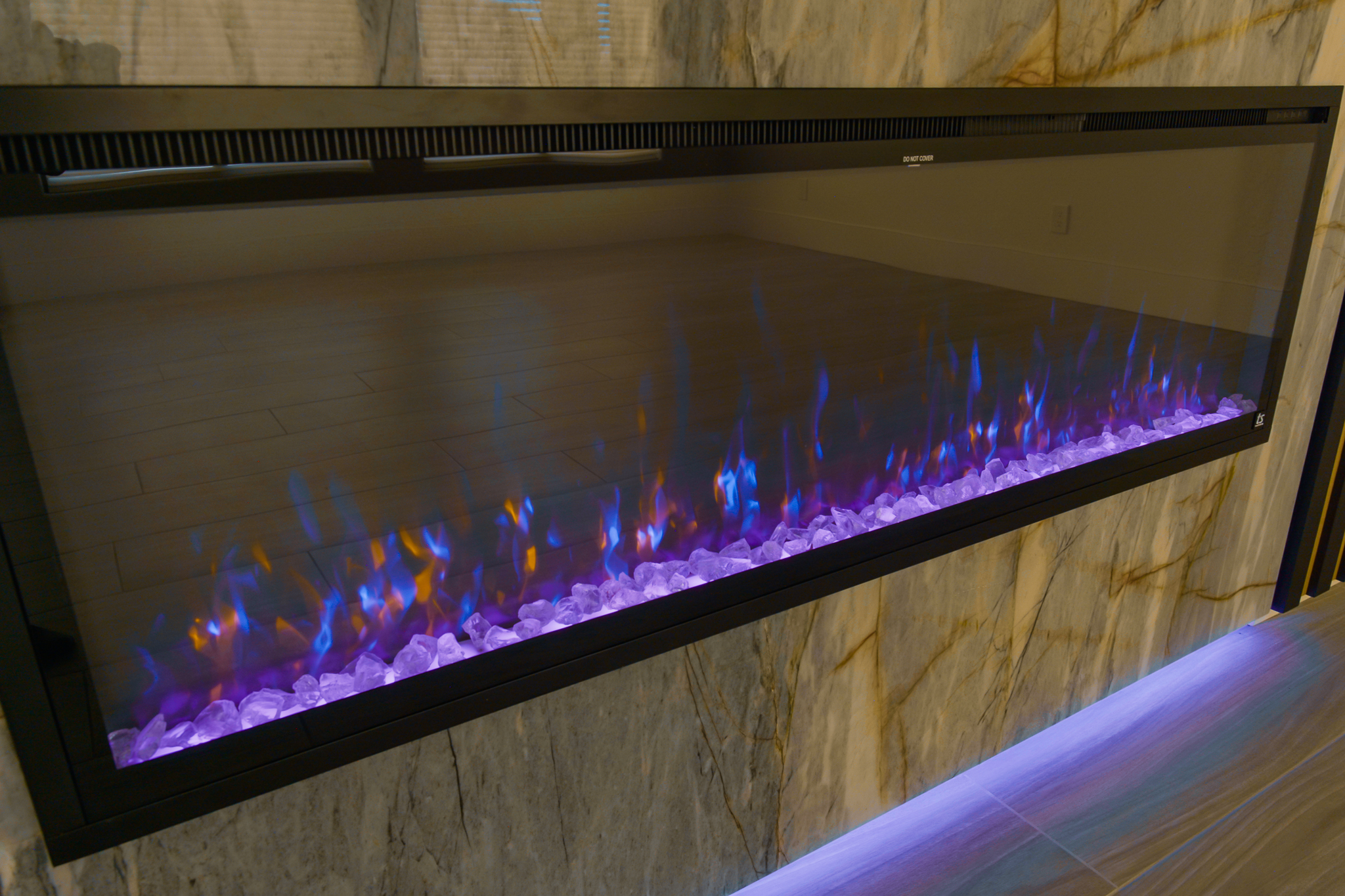Modern black electric fireplace mounted on a marble wall with simulated flames.