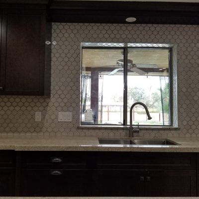 Contemporary Mesa kitchen detail featuring dark brown cabinetry, a stainless steel sink, a chrome faucet, a light countertop, and a decorative mosaic backsplash with a view outside.
