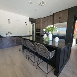 Modern Kitchen Remodel by Five40 Remodeling LLC in Mesa, AZ A newly remodeled modern kitchen featuring a large black island with four woven black bar stools, dark brown cabinetry, light wood-look tiled flooring, and a textured white accent wall, with a large stainless steel refrigerator.