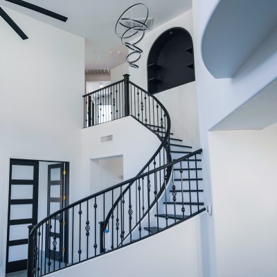 Elegant wrought iron spiral staircase in a bright, two-story entryway of a Tempe home, illuminated by an Artemide Alphabet of Light chandelier.