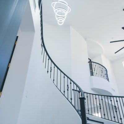 View up a two-story entryway in a Tempe home featuring a modern LED chandelier and a large black Minka-Aire Xtreme H2O ceiling fan.