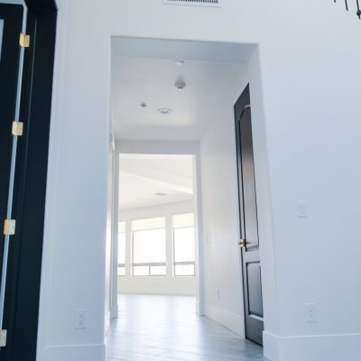 Modern interior hallway with white walls, light flooring, and a partially visible black patterned door.