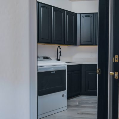 Laundry space with a white Maytag dryer, sleek black cabinets, light countertops, and a black Kraus Bolden faucet.