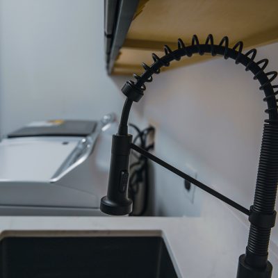 Modern black pull-down kitchen faucet over a dark sink, with a washing machine in the background.