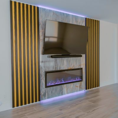 Living space with a stone and wood slat accent wall, housing a TV and electric fireplace with purple flames.